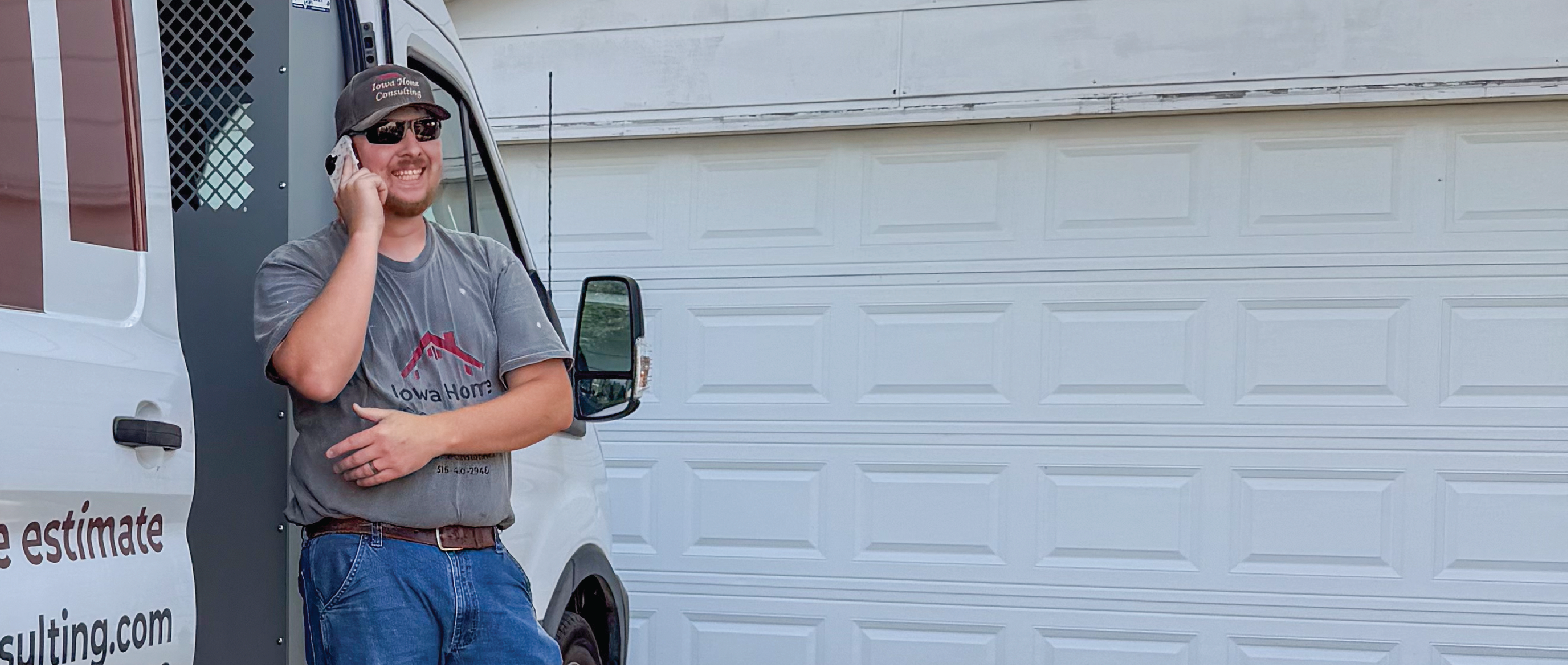 Iowa Home Consulting handyman checking in with team over the phone standing in front of a garage